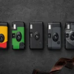 Five disposable cameras lined up on a dark surface, including Kodak FunSaver, Fujifilm QuickSnap, and Ilford single-use cameras