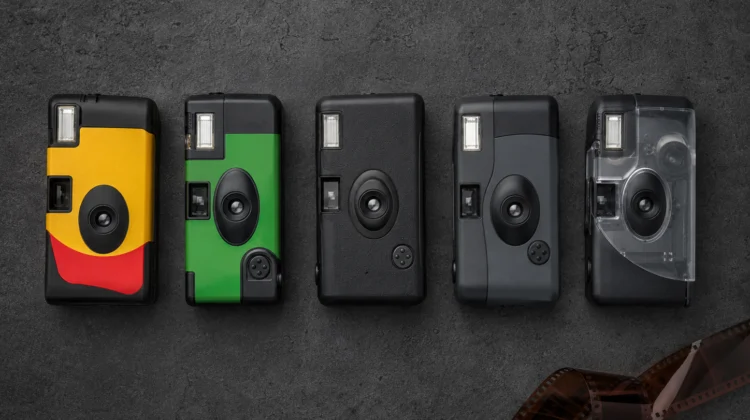 Five disposable cameras lined up on a dark surface, including Kodak FunSaver, Fujifilm QuickSnap, and Ilford single-use cameras