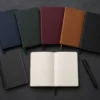 Flat lay of multiple hardcover and softcover journals lined up on a dark desk surface, showing different sizes and covers