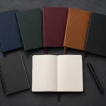 Flat lay of multiple hardcover and softcover journals lined up on a dark desk surface, showing different sizes and covers
