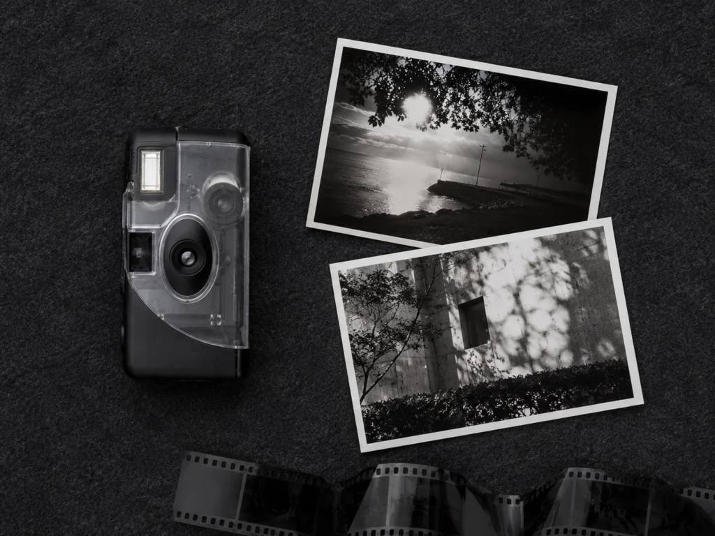 Black and white photograph printed from Ilford XP2 film lying beside the Ilford single-use camera on a dark surface