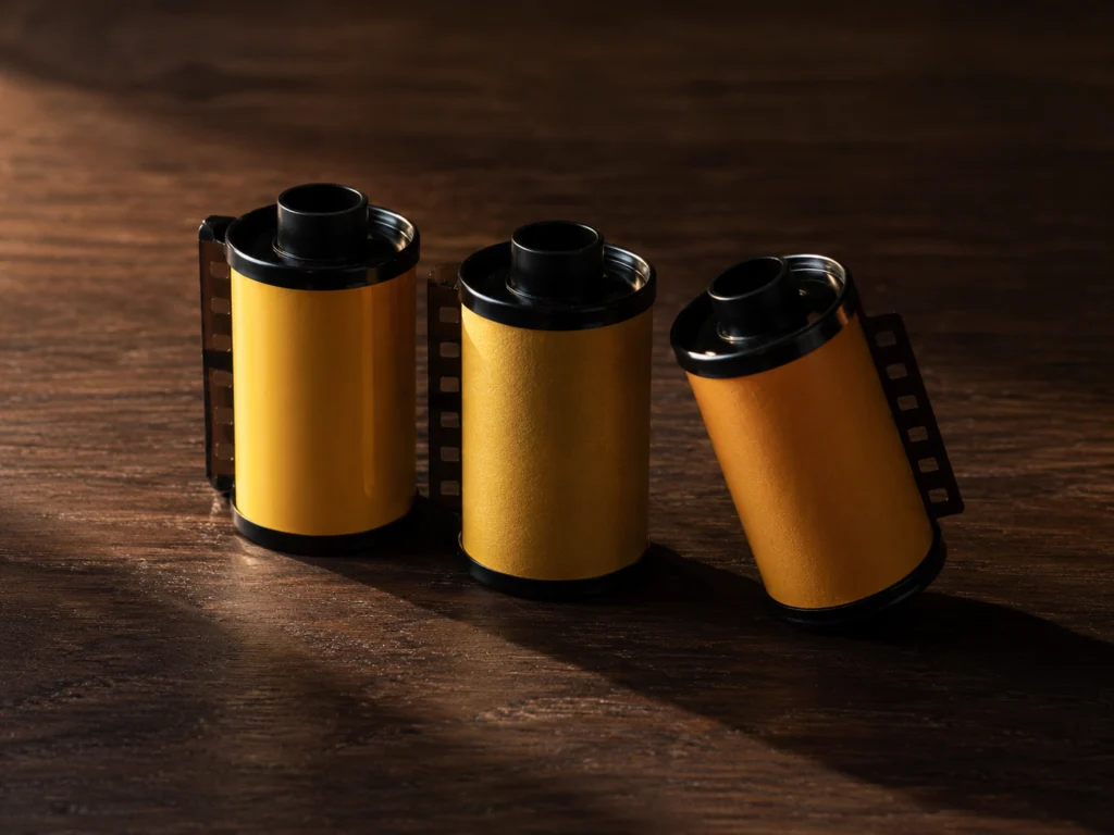 Three rolls of 35mm color film in yellow packaging standing upright on a dark wooden surface, showing film canister tops