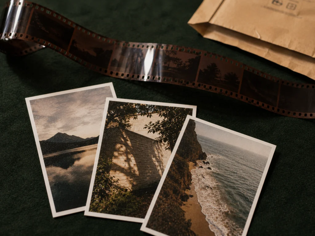 Strip of 35mm color film negatives held up against light, with a few printed film photographs spread on a dark surface below